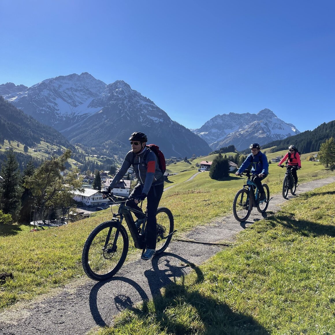 Drei Radfahrer auf E-Bikes genießen eine sonnige Berglandschaft. © Walser BikeTours
